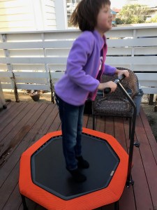 Picture of a young girl jumping on a mini-trampoline, holding onto the handle.